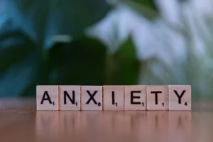 Wooden letter tiles spell out the word “anxiety” on a tabletop with a softly blurred green background.