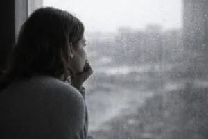 Person looking out a rain-streaked window in a quiet, contemplative moment, representing anxiety and uncertainty.