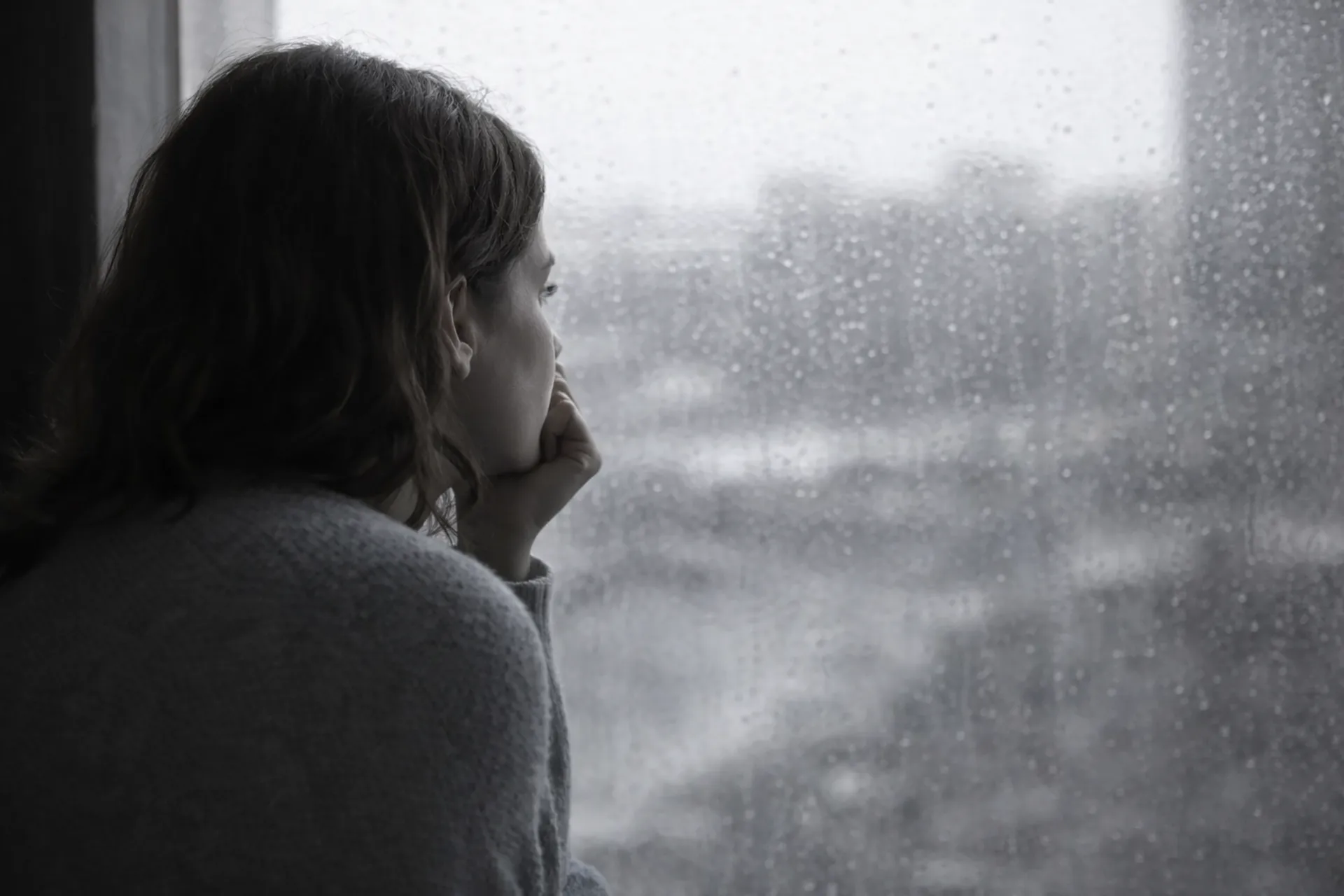 Person looking out a rain-streaked window in a quiet, contemplative moment, representing anxiety and uncertainty.